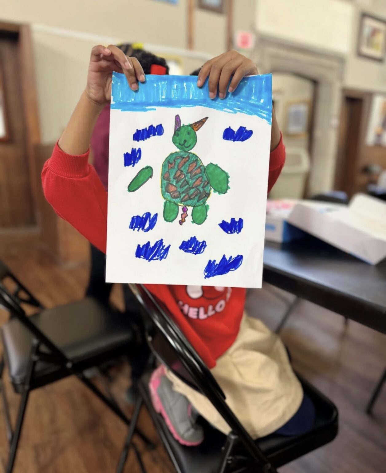 A child holding up a drawing of a turtle
